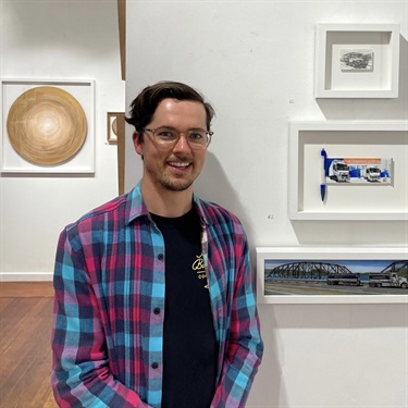 Zachariah Fenn standing in front of a collection of his mixed media artworks from the exhibition 